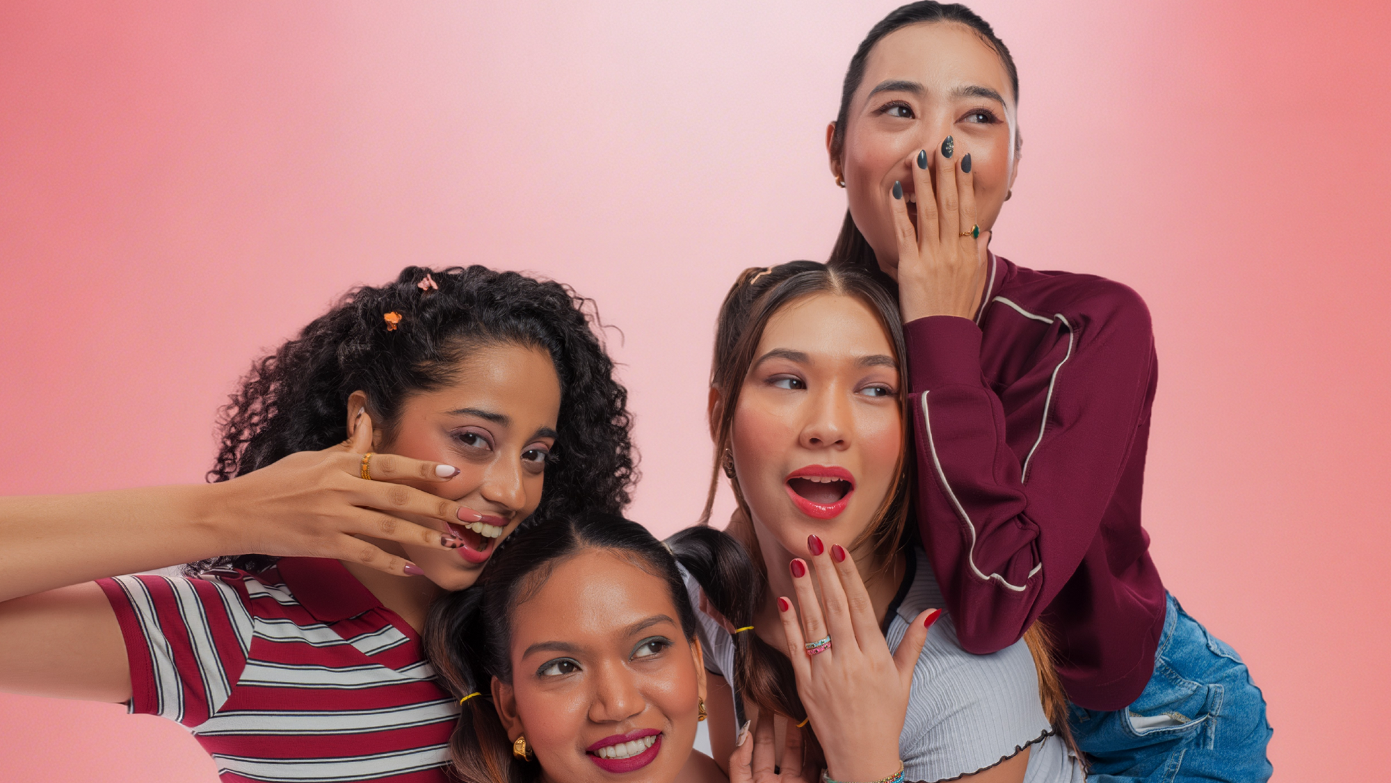Four women posing playfully against a pink background